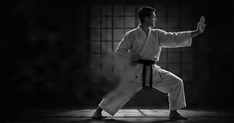 Kata: ein Karateka in einer tiefen Stellung; der schwarze Gürtel ist vorn gebunden.